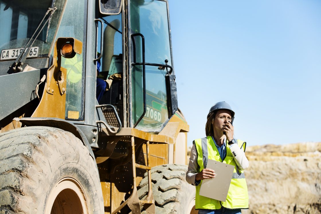 emale architect using walkie-talkie by bulldozer at quarry against clear sky